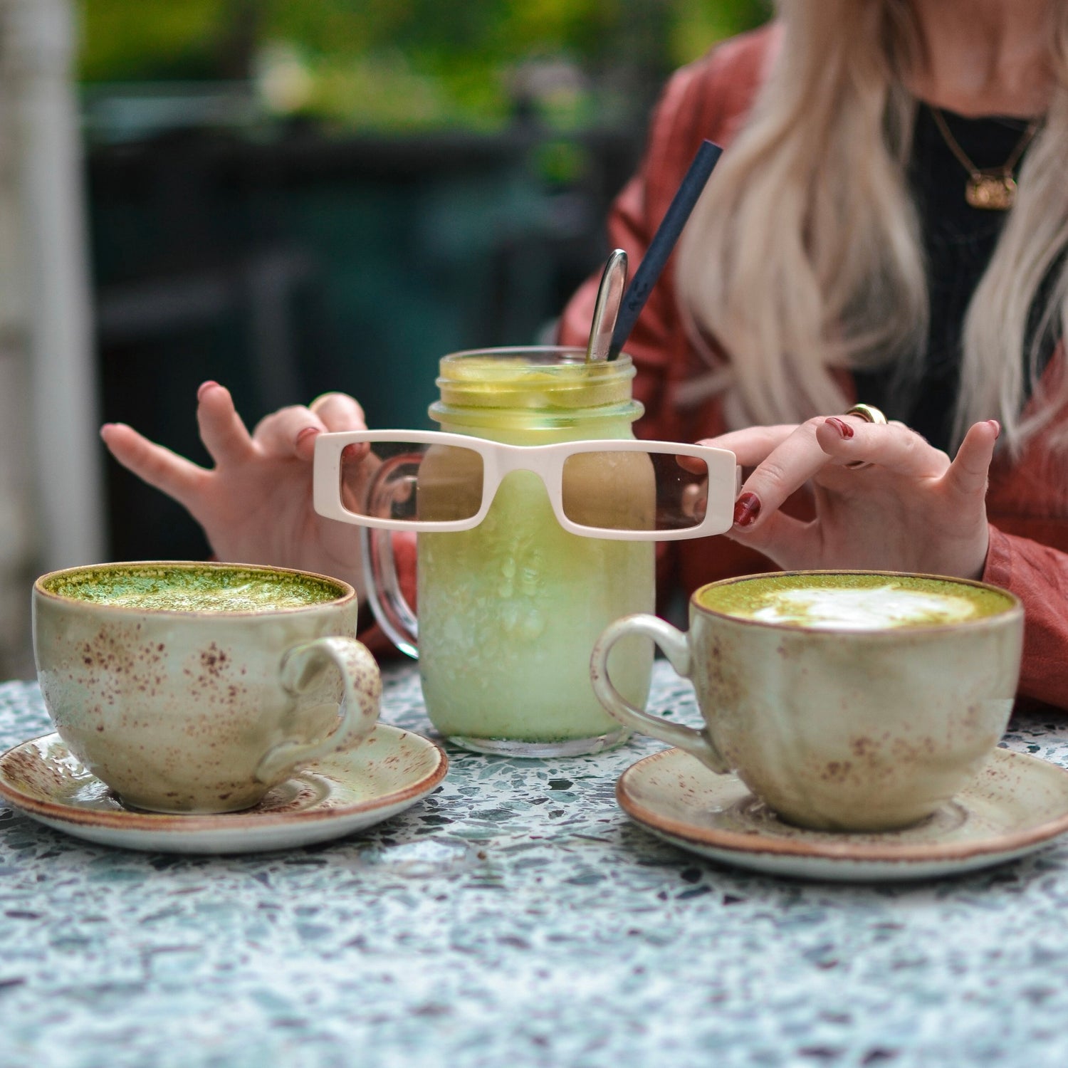 Two cups of green tea and a glass with a straw on a table, with a person in the background.
